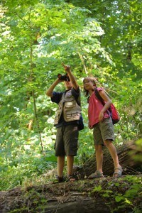 Two children in woods looking through binoculars.