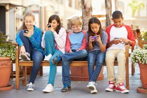 Group Of Children Sitting In Mall Using Mobile Phones